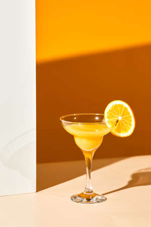 Graphic still life of single cocktail glass with fresh orange juice against abstract background with high shadowsの写真素材