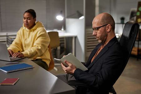Side view portrait of bald mature businessman reading document at team meeting in office, copy space