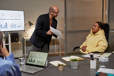 Portrait of mature business manager presenting project to diverse team during meeting in office