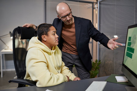 Side view portrait of mature business manager instructing female employee and pointing at computer...