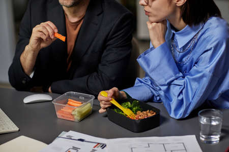 Close up of two business people eating takeout at desk together while working late at night, copy spaceの写真素材