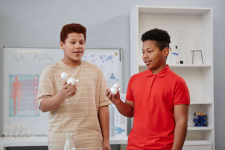 Waist up portrait of two teenage boys holding molecule models while giving presentation in chemistry...