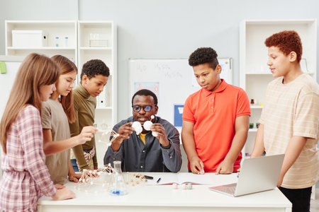 Front view at diverse group of children standing by African American teacher in chemistry class at...