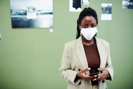 Young African American woman wearing elegant outfit and mask on face standing in modern art gallery...