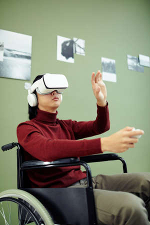 Young Asian man with disability wearing VR headset visiting contemporary photography exhibition in modern art gallery using augmented reality technologyの写真素材