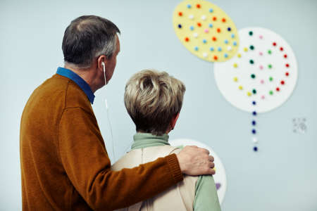 Back view of senior couple looking at picture having audio tour at exhibition in contemporary art galleryの写真素材