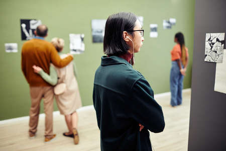 Ethnically diverse people looking at contemporary black and white photos on walls at modern photography exhibition in galleryの写真素材