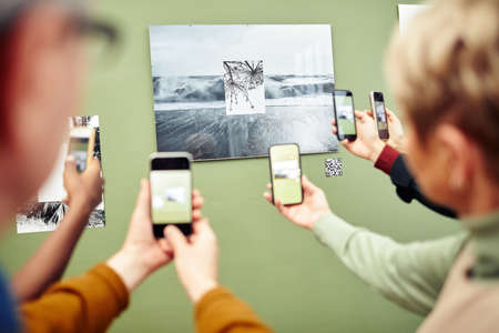 Unrecognizable people scanning QR code using smartphones to get more information about photo on wall at exhibitionの写真素材