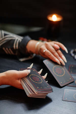 Vertical closeup of unrecognizable black woman reading tarot cards over table in fortune tellers shopの写真素材