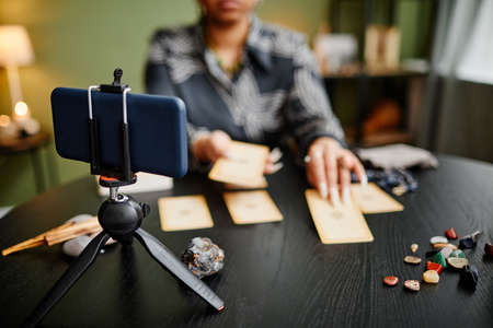 Close up woman doing tarot reading online with smartphone camera in foreground, copy space