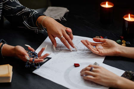 Close up of fortune teller pointing at astrology chart during spiritual seance with young womanの写真素材