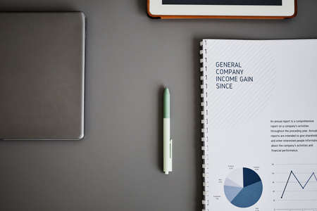 Minimal flat lay of business tools on grey desk, focus on pen and finance notebook