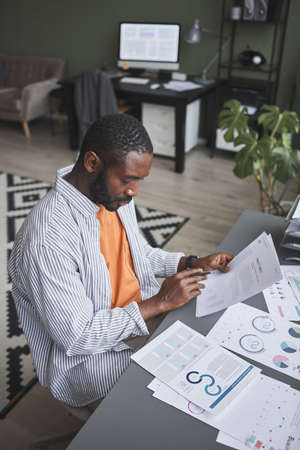 Vertical portrait of modern black businessman working at home and analyzing documents with dataの写真素材