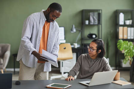 Portrait of African American man talking to Asian colleague asking advice on project in office