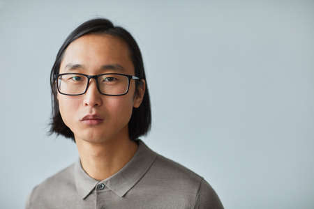 Minimal close up portrait of young Asian businessman wearing glasses and looking at camera while...