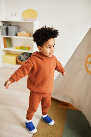 Vertical full length portrait of cute African American boy wearing minimal trendy outfit while...