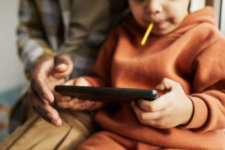 Close up of black father and little boy using smartphone together and watching cartoons online, copy...