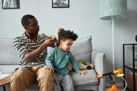 Portrait of young father brushing hair of cute little boy while taking care of son indoors, copy spaceの写真素材