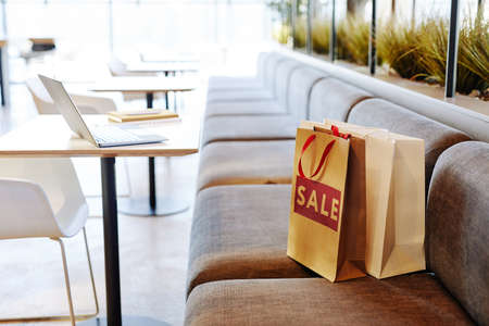 Background image of paper shopping bags with red SALE sign on seat in empty food court at shopping mall, copy spaceの写真素材