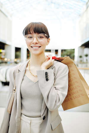 Vertical waist up portrait of elegant young woman holding shopping bags in mall and wearing glasses