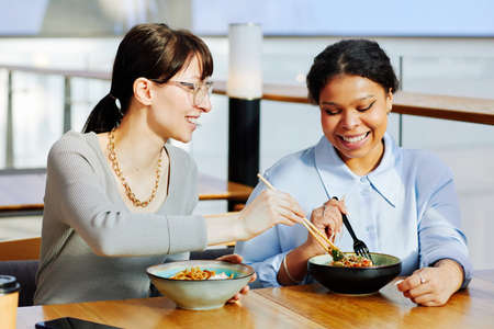 Portrait of two young girls enjoying Asian food in cafe and sharing meal smiling happily