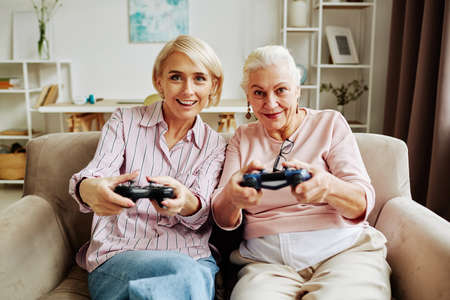 Front view portrait of white haired senior woman playing video games with adult daughter in cozy home sceneの写真素材