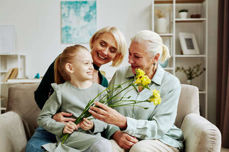Portrait of smiling little girl giving flowers to grandmother on Mothers day in cozy home sceneの写真素材