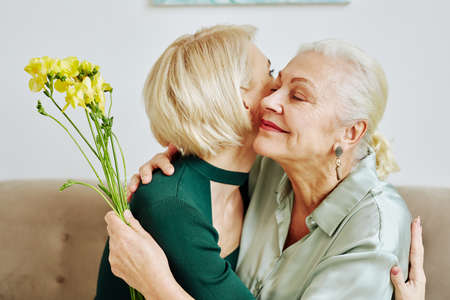 Side view portrait of adult daughter embracing mother and giving her flowers on Mothers dayの写真素材
