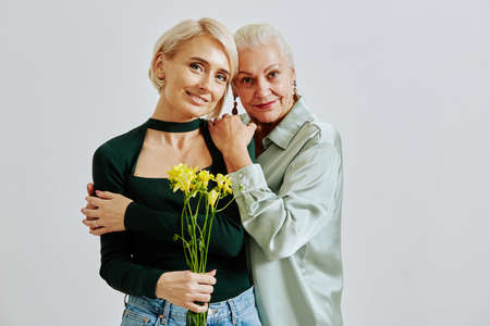 Minimal waist up portrait of senior woman with adult daughter holding flowers and looking at camera, copy spaceの写真素材