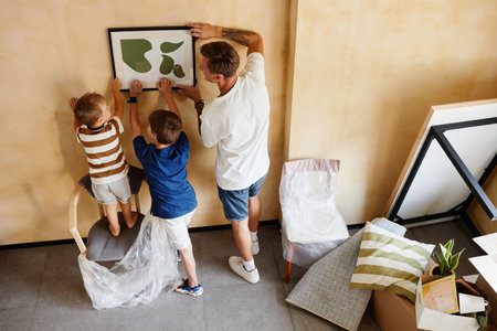 Top view portrait of father with two sons hanging picture on wall together while moving to new home, copy spaceの写真素材