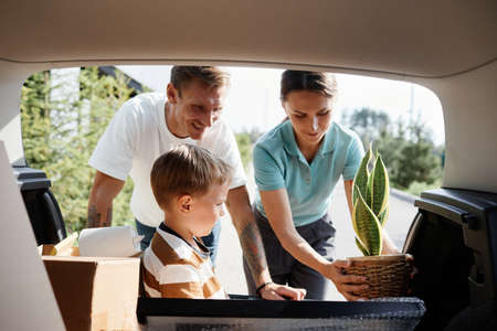 Portrait of smiling family loading boxes in car trunk while moving into new house in sunlightの写真素材