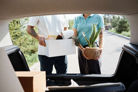 Cropped shot of couple loading boxes in car trunk while moving into new house scene in sunlight