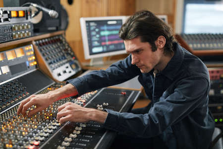 Side view portrait of music producer using digital audio workstation in professional recording...