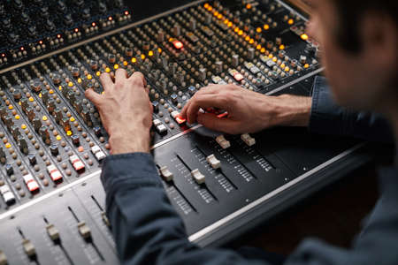 Close up of male hands operating buttons and toggles at digital audio workstation in recording studio, music production conceptの写真素材