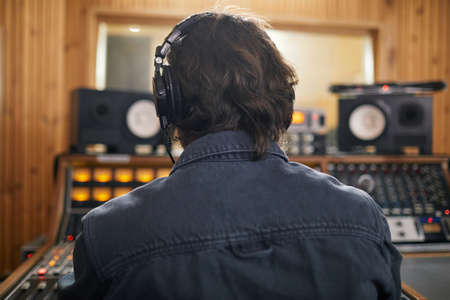 Back view of man wearing headphones at audio workstation in professional recording studio, copy spaceの写真素材