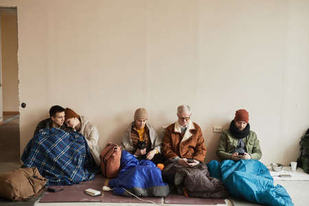Minimal front view at diverse group of refugees hiding in shelter together during war or crisis, copy spaceの写真素材
