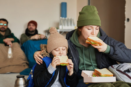 Portrait of Caucasian young mother and son eating sandwiches in refugee shelter during war or crisis, copy spaceの写真素材