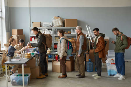 Side view at group of people standing in line at help and donations center for refugees, copy space