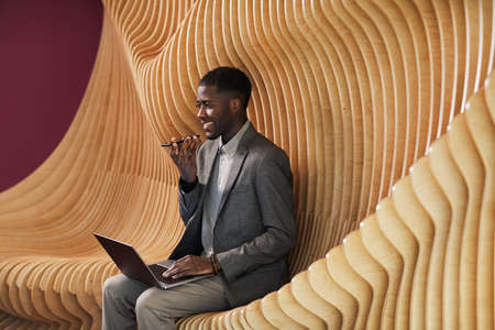 Graphic portrait of smiling black businessman recording voice message while working at modern office...