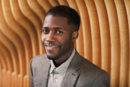 Graphic portrait of smiling black businessman looking at camera in modern office space with wooden panelling, copy spaceの写真素材