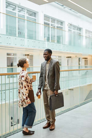 Full length portrait of two coworkers chatting at balcony in office building with modern...