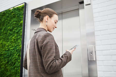 Minimal low angle shot of young businesswoman waiting for elevator in modern office building and...