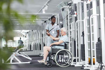 Side view portrait of senior man in wheelchair doing exercises in gym at rehabilitation clinic, copy...