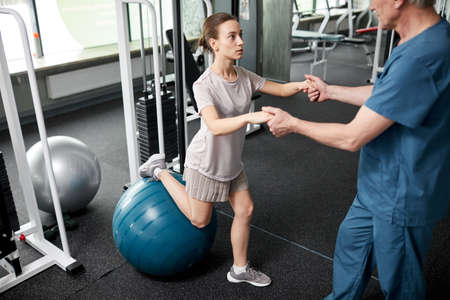 High angle portrait of young woman doing rehabilitation exercises in gym at physiotherapy clinic...