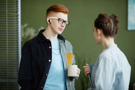 Side view portrait of creative man and woman chatting while discussing work in vibrant green officeの写真素材