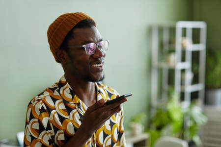 Vibrant side view portrait of black young man using smartphone and wearing creative style against greenの写真素材