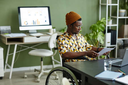Portrait of black young man in wheelchair wearing creative style while working in office, copy spaceの写真素材