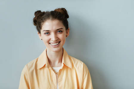 Minimal portrait of cheerful young woman with genuine smile looking at camera against blue wall, copy spaceの写真素材
