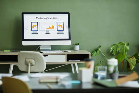 Background image of office workplace and computer screen with data against green wallの写真素材