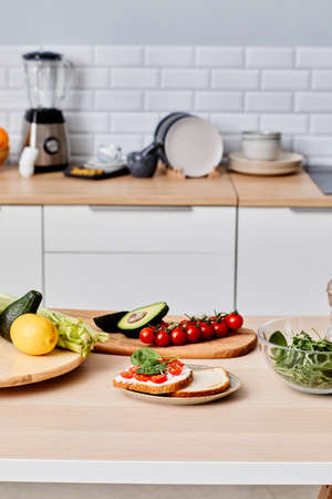 Fresh vegetables on cutting board on table for preparing sandwiches and salad in domestic kitchenの写真素材